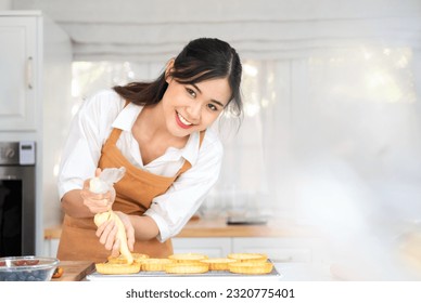 Small business entrepreneur asian woman bakery shop making fruit tart. Female Baker Using Piping Bag Decorate fruit tart with cream cheese on white Bright kitchen counter.indoor lifestyle concept. - Powered by Shutterstock