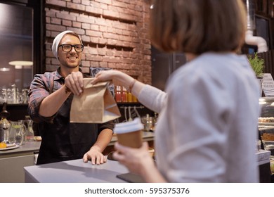 Small Business, Food, People And Service Concept - Happy Female Customer With Coffee Cup Taking Paper Bag From Man Or Barman At Vegan Cafe