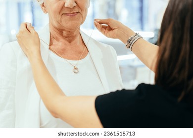 Small business, jewelry store concept. Grey haired senior lady tries on necklacer in jewelry store. Unrecognizable elderly woman try pendant. Female owner showing necklace to woman customer. - Powered by Shutterstock