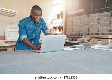 Small Business Owner Of African Descent Using Laptop In Workshop