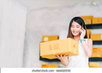 Small Business Owner, Asian Woman Hold Package Box, Using Mobile Phone Call Receiving Purchase Order, Working At Home Office. Online Marketing Delivery, Startup SME Entrepreneur Or Freelance Concept.