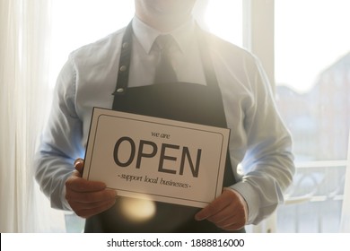 Small Business Owner holding sign for restaurant during lockdown - Coronavirus pandemic takeout service at local café - Restaurant open during lockdown - Small local food business owner takeaway sign - Powered by Shutterstock