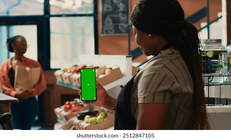 Small business owner looking at phone with greenscreen in local grocery store, showing blank copyspace layout on smartphone. Vendor selling her homegrown produce at farmers market. - Powered by Shutterstock