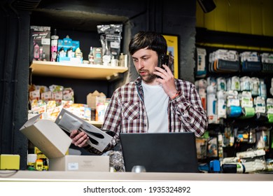 Small Business Owner On Phone And Computer In Store. Sport Shop Worker Making Call With Cell Phone. Salesman Working And Talking On Cell Phone In Bicycle Shop. Seller Taking Orders By Phone.