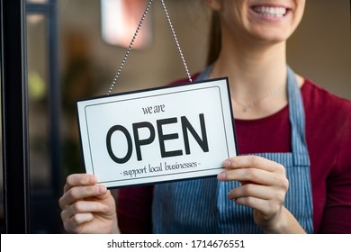 Small business owner smiling while turning the sign for the reopening of the place after the quarantine due to covid-19. Close up of woman’s hands holding sign now we are open support local business. - Shutterstock ID 1714676551