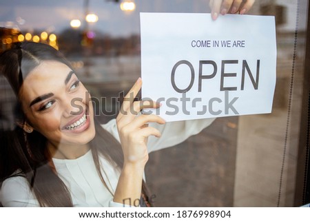 Small business owner smiling while turning the sign for the reopening of the place after the quarantine due to covid-19. Close up of woman’s hands holding sign now we are open support local business.