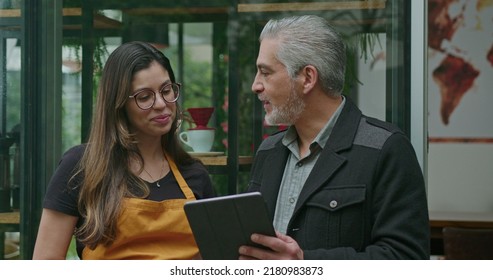 Small Business Owner Speaking With Female Employee Barista Wearing Apron. Boss Manager Talking With Staff Explaining Restaurant Business Holding Tablet Device