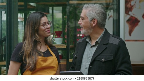 Small Business Owner Speaking With Female Employee Barista Wearing Apron. Boss Manager Talking With Staff Explaining Restaurant Business Holding Tablet Device