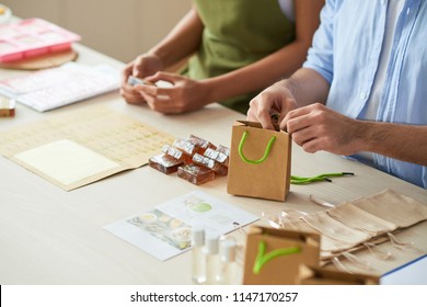 Small Business Owners Filling Shopping Bags With Natural Soaps And Booklets