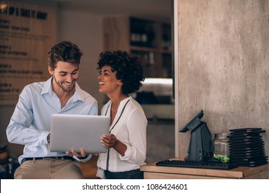 Small Business Owners Using Laptop In Their Restaurant. Smiling Man And Woman Working In Their Restaurant.