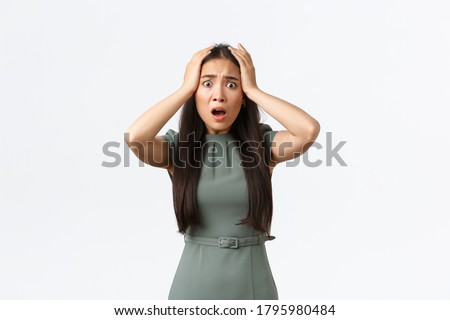 Small business owners, women entrepreneurs concept. Shocked asian woman in panic, grab head and looking startled with concerned alarmed face, being robbed, standing white background
