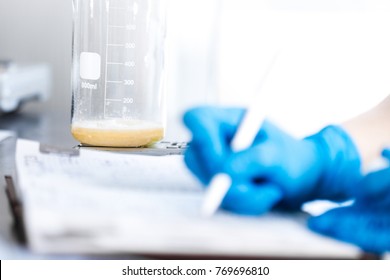 Small business people at work. Working process in laboratory of cosmetic production. Mixing components. Close-up hands of technologist making notes in paper notepad.