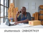 Small Business Startup, SME Owner, American Male Entrepreneur Africans use smartphones and Laptop takes orders and checks online orders to prepare boxes to sell to customers. Online SME business idea