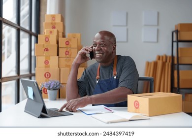 Small Business Startup, SME Owner, American Male Entrepreneur Africans use smartphones and Laptop takes orders and checks online orders to prepare boxes to sell to customers. Online SME business idea - Powered by Shutterstock