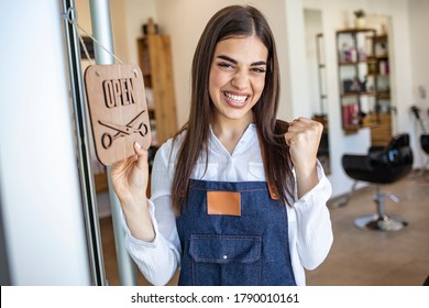 Small business survival after covid-19 pandemic. Portrait of smiling trendy 30 years old small business owner woman in apron showing open sign. Opening small business after covid-19 pandemic.