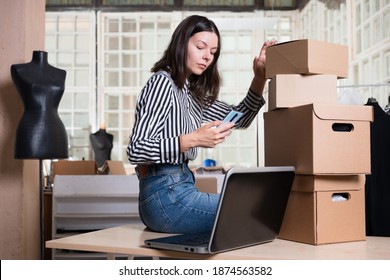 Small Business, Tailor Shop, Costume Designer's Workshop. A Young Woman Entrepreneur In The Workplace Is The Packaging Of The Parcel And Uses The Phone For Business Contacts. Portrait In The Interior