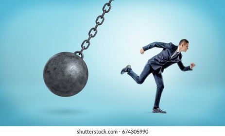 A small businessman running away from a giant black wrecking ball on a chain. Business trouble. Leaving problems behind. Run away from crisis.