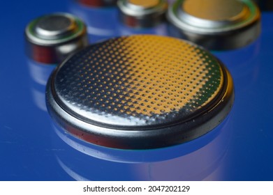 small button batteries of different sizes, highlighted in red and orange, lie against a blue background. close-up.