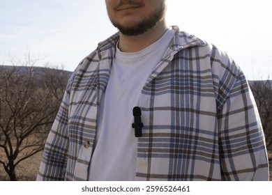 Small buttonhole microphone attached to a man's blue shirt, close-up, audio equipment, microphone placement, professional gear, sound recording, podcast, broadcasting, technology