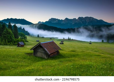 Small cabin on mountain meadow at forest edge, Geroldsee in the background Karwendel Mountains at sunrise, Kaltenbrunn, Upper Bavaria, Germany