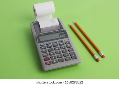 A Small Calculator With A Paper Tape And Pencils On A Green Desk Blotter