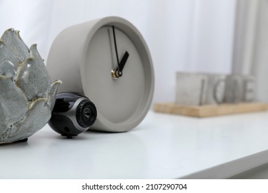 Small Camera Hidden Near Alarm Clock On White Table Indoors