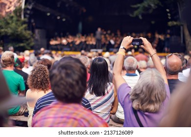 Small Cameras Capture Great Memories. Shot Of A Person In The Crowd Holding A Camera To Photograph A Classical Concert.