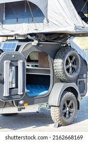 A Small Camper House On A Trailer Car With A Solar Battery And A Folding Tent With Sleeping Places On The Roof For Mobile Tourism.