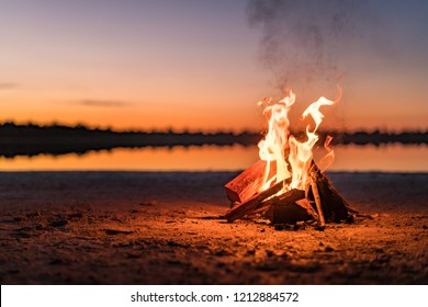 Pequeña fogata con gentiles llamas al lado de un lago durante una brillante puesta de sol. Australia Occidental, Australia.