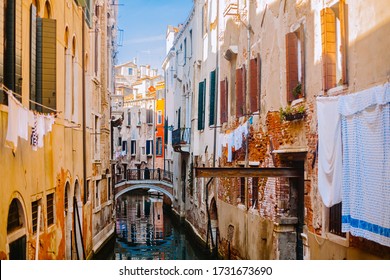 A small canal street in Venice. Old houses with Windows facing the canal. Italian flavor in Venice. Clothes drying on a clothesline in the street Tourist destination Venice, Italy. - Powered by Shutterstock