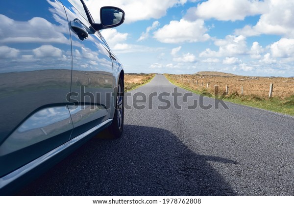 Small car parked on a\
small road. Warm sunny day. Sky and fields reflect on the car\
surface. Travel concept