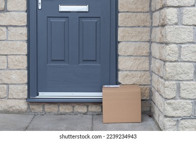 Small cardboard parcel left on the doorstep. Grey door and doorway. Courier delivery parcel.