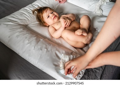Small caucasian baby girl or boy lying on the bed in bright room while hands of her mother changing diapers and clothes copy space parenting childhood concept cleaning skin wet wipe copy space