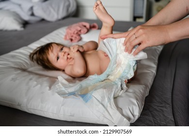 Small caucasian baby girl or boy lying on the bed in bright room while hands of her mother changing diapers and clothes copy space parenting childhood concept cleaning skin wet wipe copy space