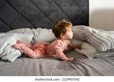 Small caucasian baby lying down on the belly on the bed with wet urine stain on the sheet and clothes looking to the side Bedwetting child pee on the bed
