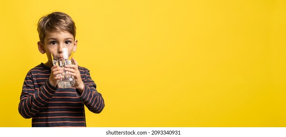 Small caucasian boy little child holding glass of water while standing in front of modern yellow background drinking and looking to the camera with copy space - Powered by Shutterstock