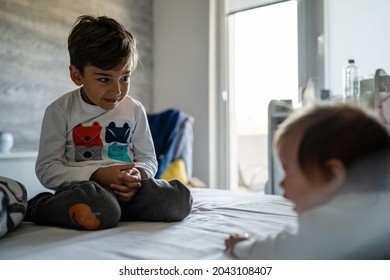 Small Caucasian Boy Taking Care Of His Baby Brother Or Sister While While Playing On The Bed At Home In Day Brotherhood And Family Growing Up Concept