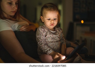 Small Caucasian Child Little Girl Toddler Mother And Daughter Sitting In Dark Room At Night At Home On Sofa Bed Watching Cartoons Or Movies On Mobile Phone Real People Family Growing Up Copy Space