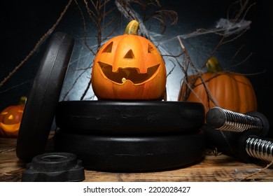 Small ceramic Halloween pumpkin on a dumbbells barbell weight plates. Healthy gym fitness lifestyle autumn or fall composition with decorative Jack-o'-lantern spooky laughing, scary head. - Shutterstock ID 2202028427