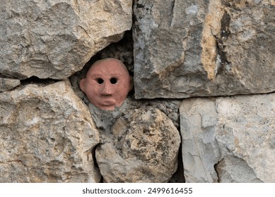 A small ceramic head peers out from a crevice in an old stone wall.