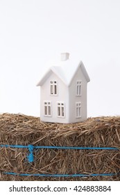 A Small Ceramic House On A Weak Foundation Of A Bale Of Hay. Great For Concepts About Foundations, Home Purchasing, Insurance, Or Other Abstract Ideas. Vertical With Copy Space.