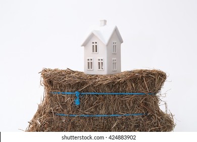 A Small Ceramic House On A Weak Foundation Of A Bale Of Hay. Great For Concepts About Foundations, Home Purchasing, Insurance, Or Other Abstract Ideas. Horizontal With Copy Space.