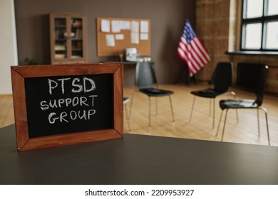 Small Chalkboard With Notice About PTSD Support Group On Table Standing Against Circle Of Several Chairs For Attendants In Studio