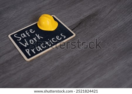 Small chalkboard with the text “Safe Work Practices” and yellow hard hat. Concepts of safety, precaution, and standards in the workplace.