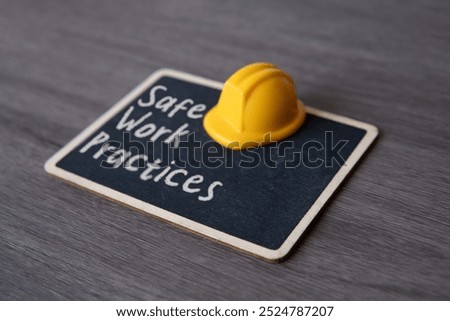 Small chalkboard with the text “Safe Work Practices” and yellow hard hat. Concepts of safety, precaution, and standards in the workplace.