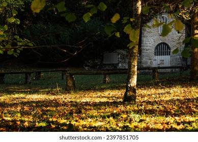 Small chapel in the forest with stone benches. Place of Christian spirituality. White chapel in the autumn forest. The autumn of the Christian religion. Pray in the forest. Church forest 