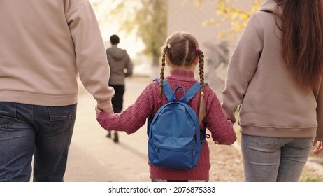 Small Child With Backpack Holds Mother And Father By Hand, Kid With Mom And Dad Walks Around Schoolyard After School, Happy Family, Rush To First Call, Primary Education, School Bag On Baby Shoulders