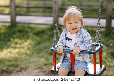 a small child with blond hair sits on a swing in the park - Powered by Shutterstock