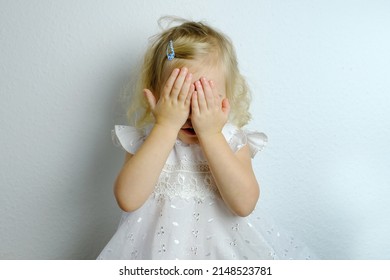 Small Child, Blonde Girl 2 Years Old In White Dress Covered Her Eyes With Her Hands From Resentment, Concept Of Children's Whims, Parental Abuse, Psychological Violence, Difficult Childhood