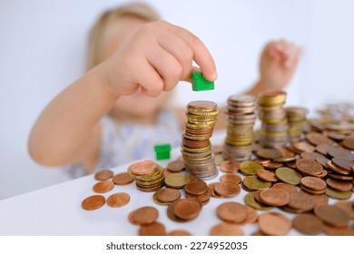 small child, blonde girl 3 years old playing with cash, house model on stacks euro currency coins, pocket money, concept home mortgage, home insurance, financial literacy of children, personal savings - Powered by Shutterstock